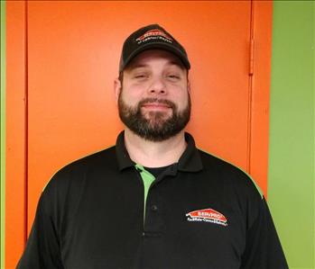 photo of male employee with brown hair and beard smiling in front of orange door.