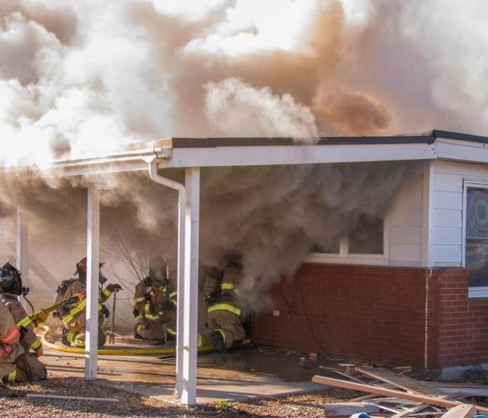 Fire fighters crouch low to avoid heavy smoke as they prepare to enter a burning home.